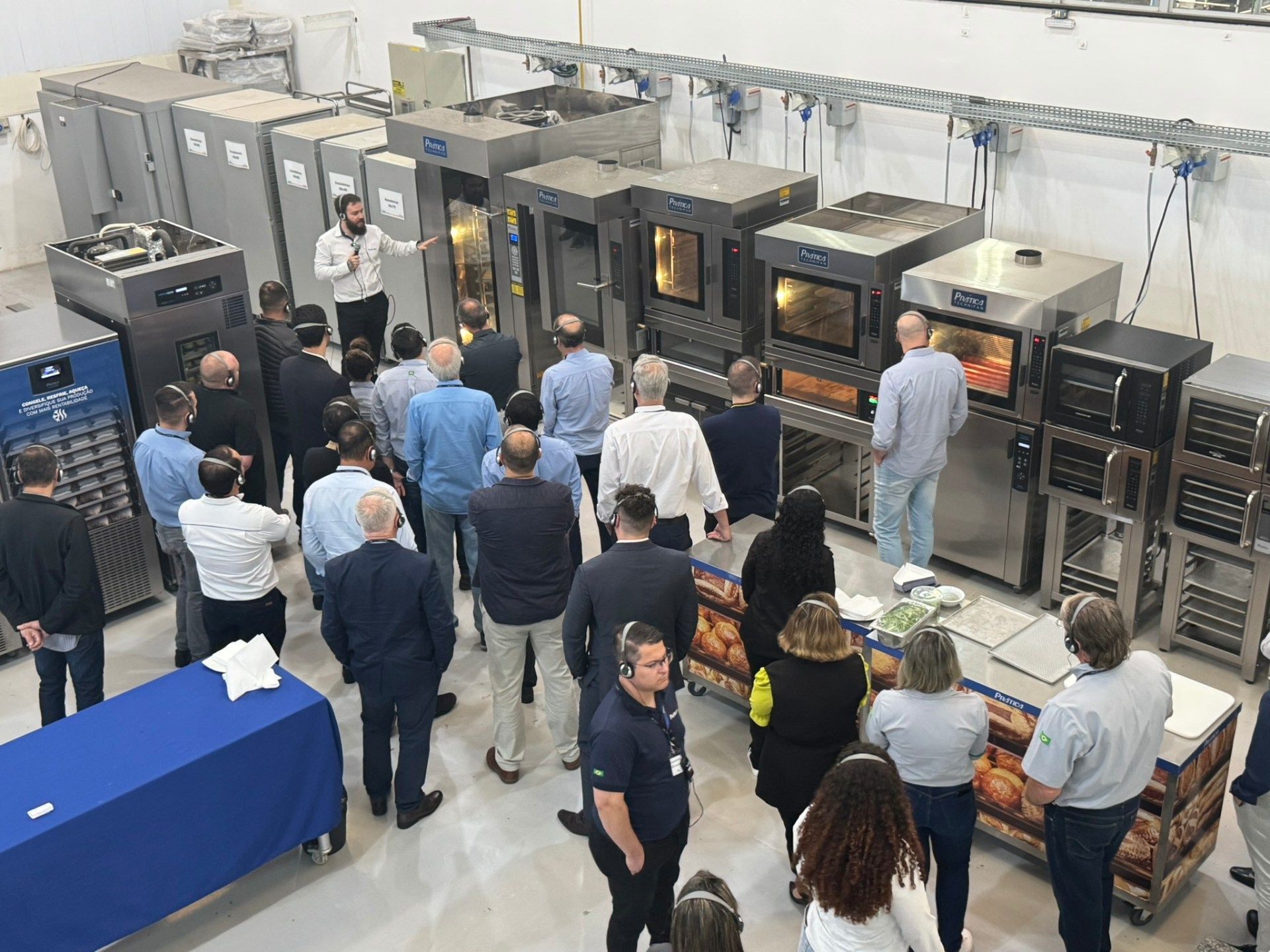 Um grupo de pessoas está em pé em frente a uma fileira de fornos.