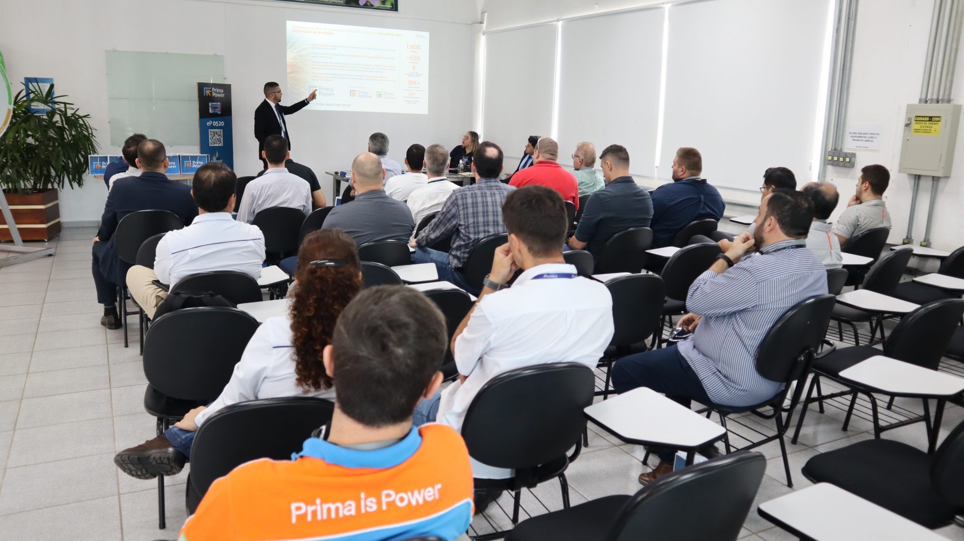 Um grupo de pessoas está sentado em uma sala de aula assistindo a uma apresentação.