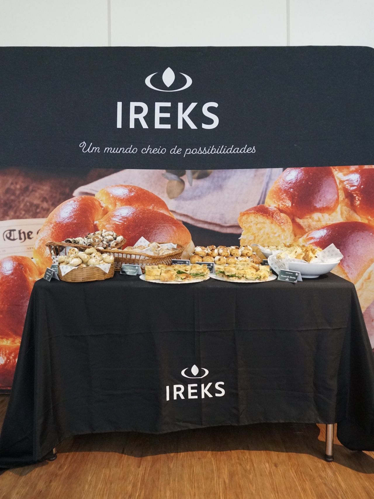Mesa com vários pães e doces, com o logotipo da IREKS, sobre um fundo preto.