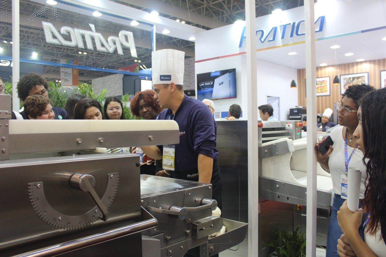 Um homem com chapéu de chef está diante de uma máquina.