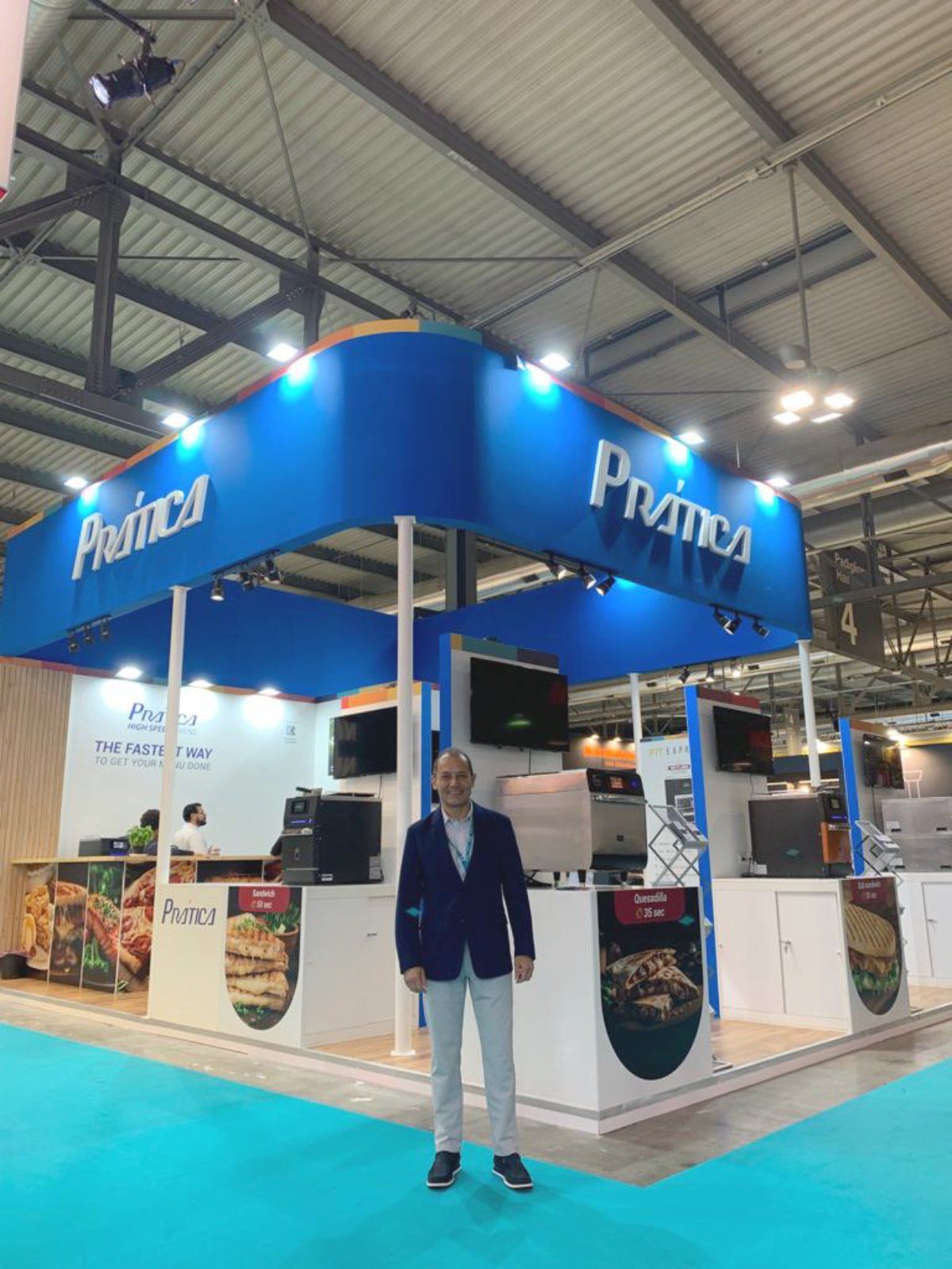 Um homem de terno está parado em frente a um estande de pramica