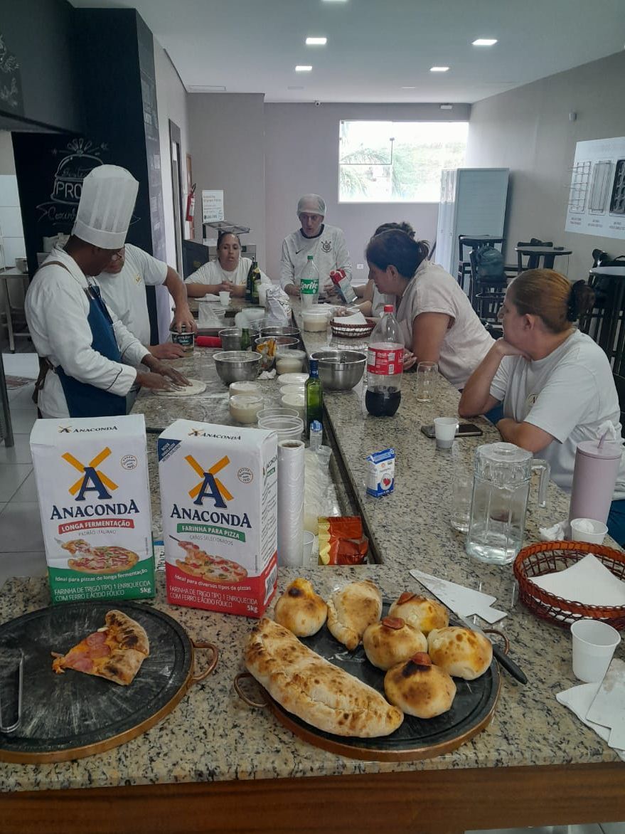 Um grupo de pessoas está sentado ao redor de uma mesa fazendo pizza.