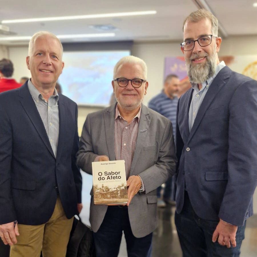Três homens estão posando para uma foto e um deles está segurando um livro