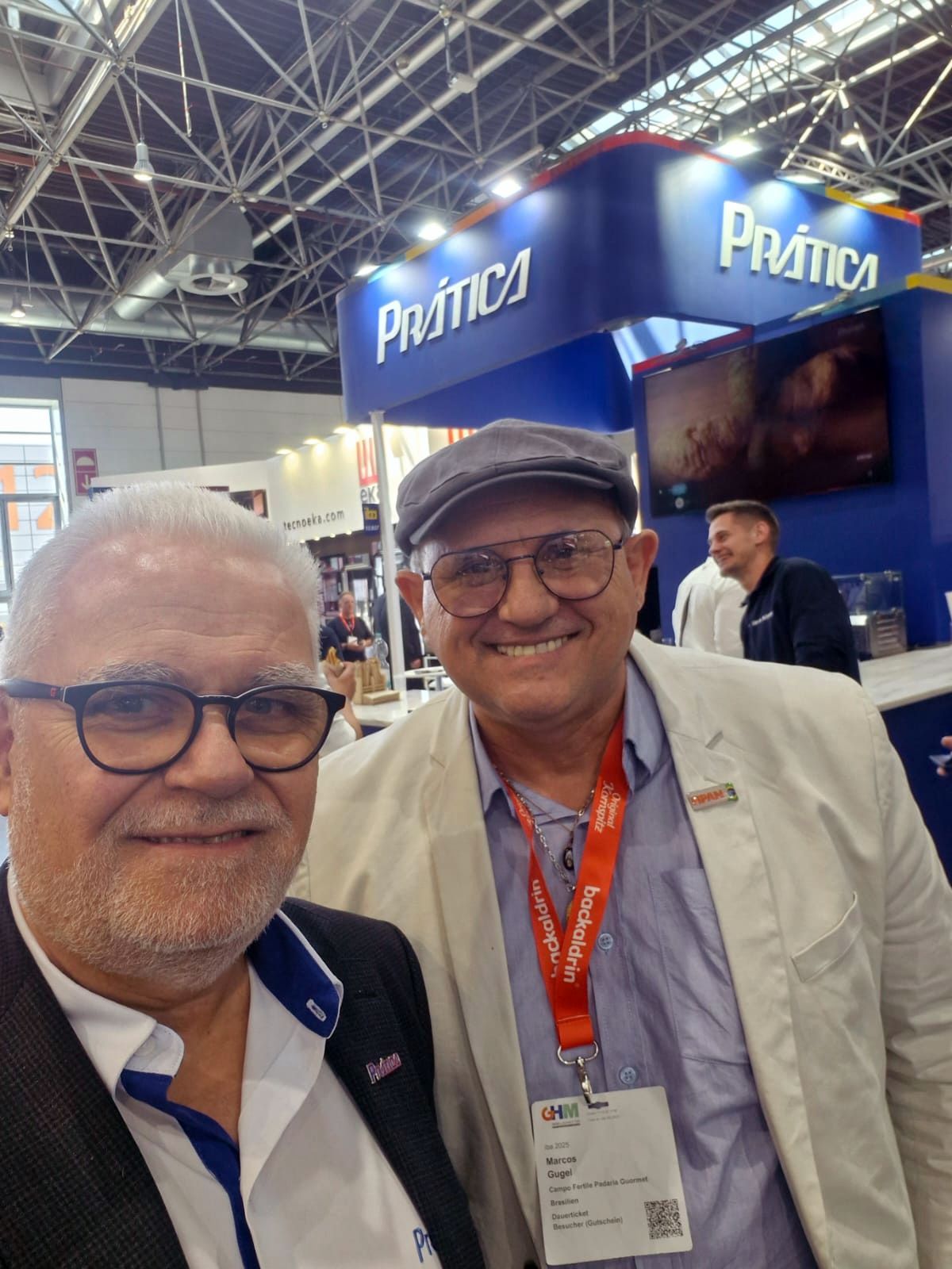 Dois homens estão posando para uma foto em frente a uma cabine de prática