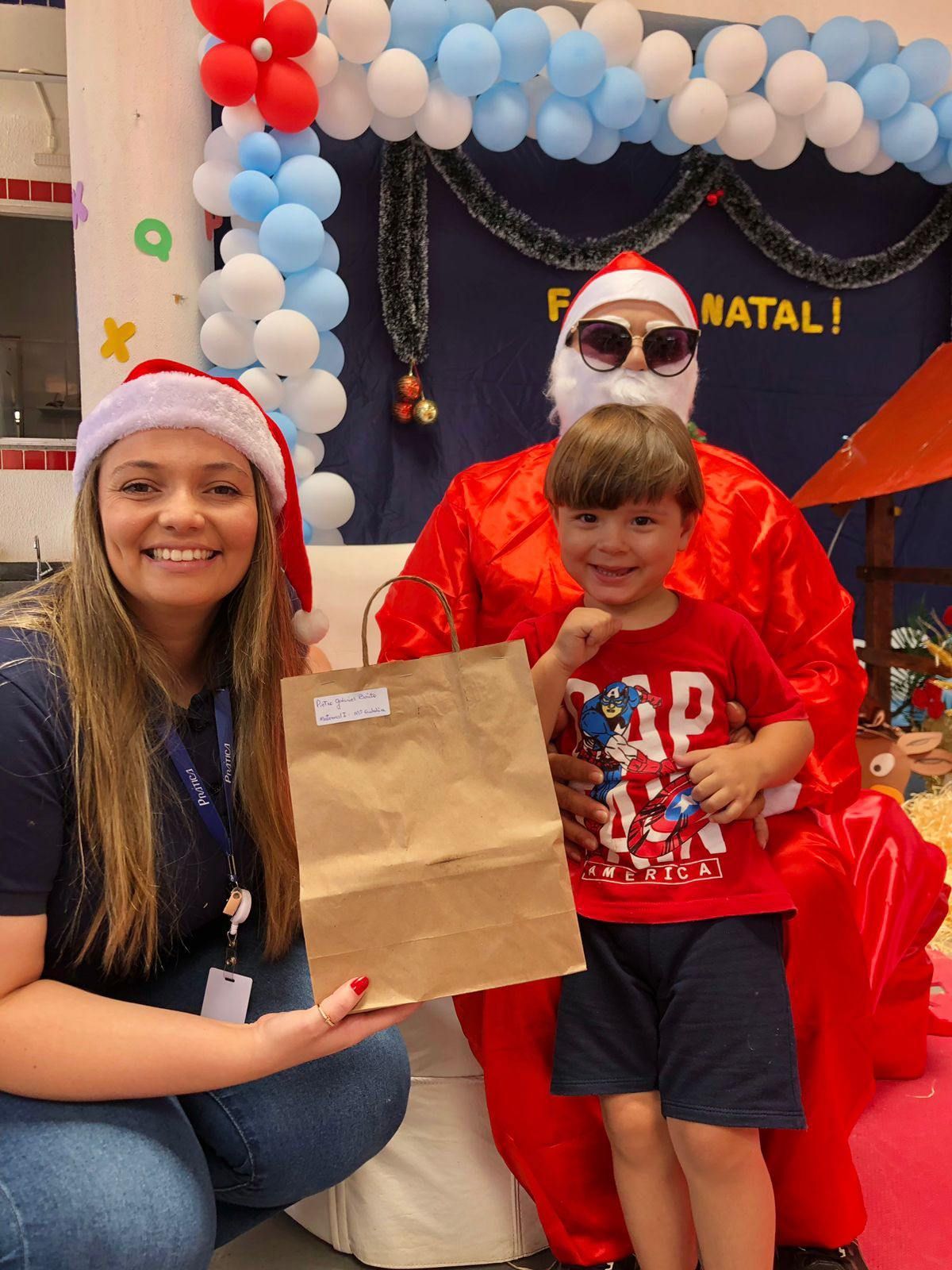 Uma mulher está segurando uma sacola marrom ao lado de um menino vestido de Papai Noel.