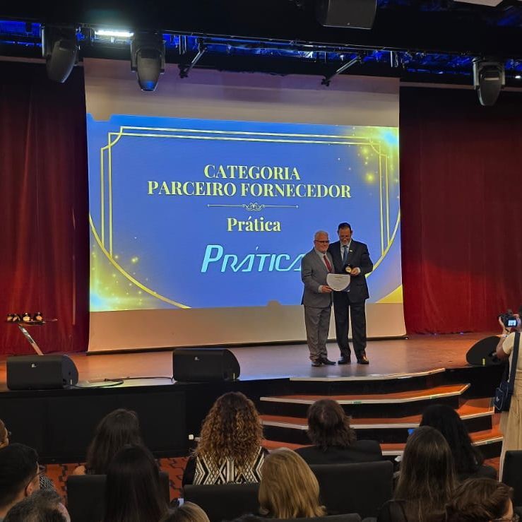 Dois homens estão em pé em um palco em frente a uma tela grande que diz