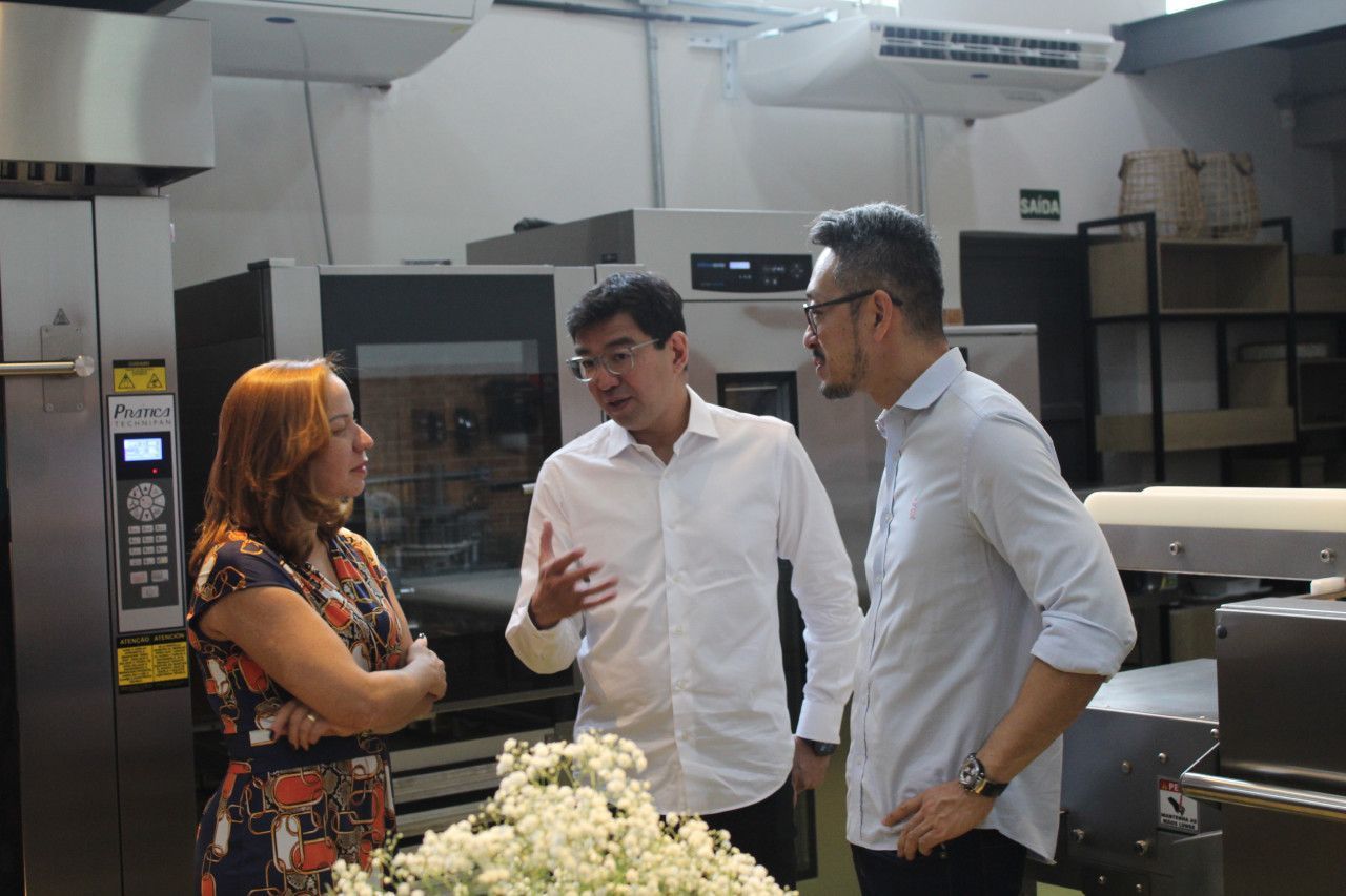 Três pessoas estão em uma cozinha conversando entre si.