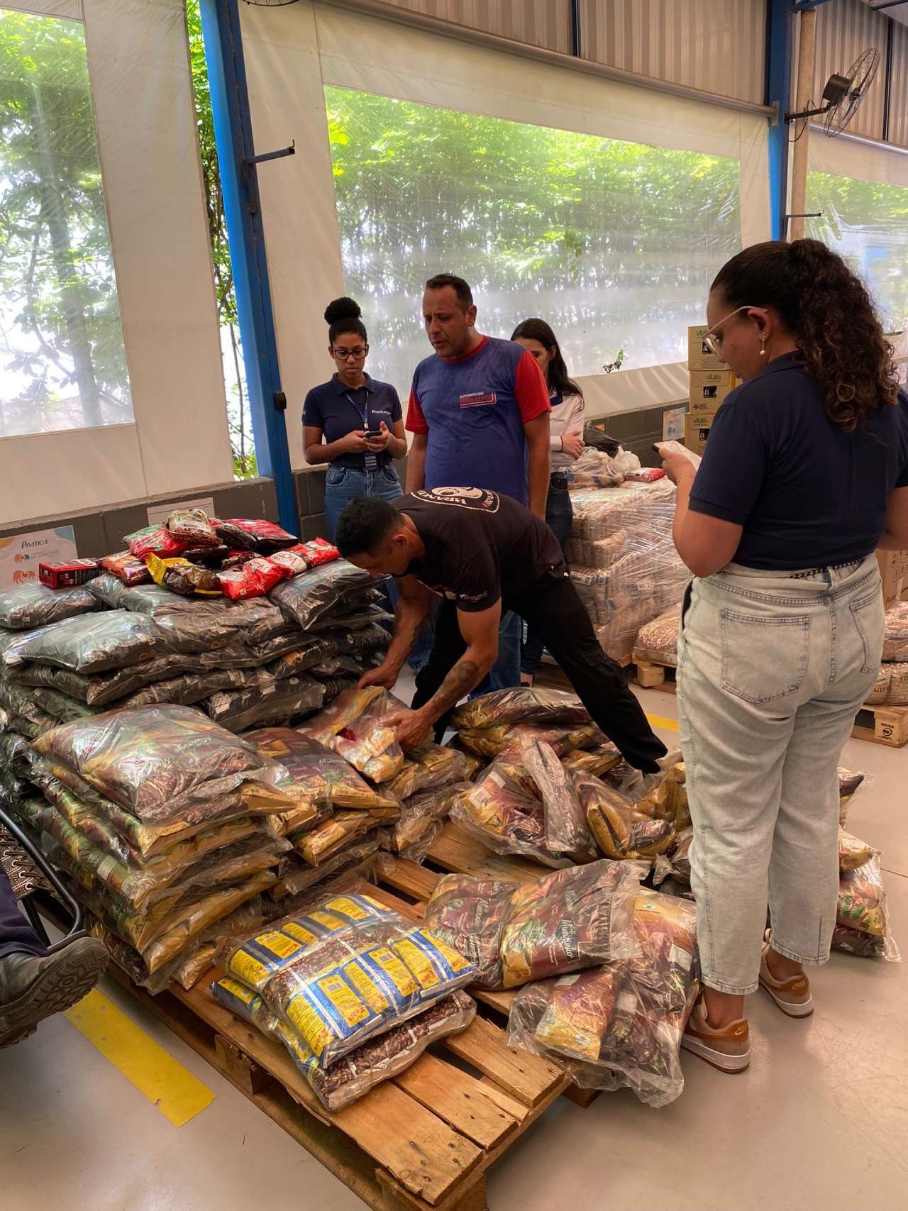 Um grupo de pessoas está em pé ao redor de uma pilha de sacos de comida.