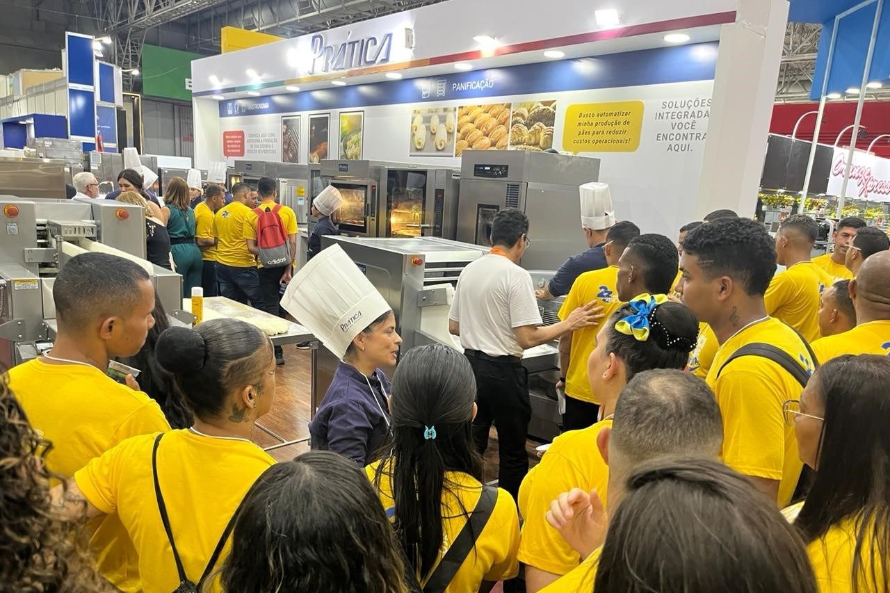 Um grupo de pessoas com camisas amarelas está em frente a uma padaria.