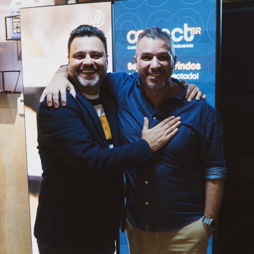 Dois homens estão posando para uma foto em frente a uma placa que diz cb