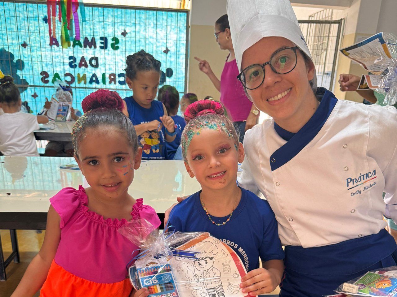 Uma mulher com um chapéu de chef está posando para uma foto com duas meninas.