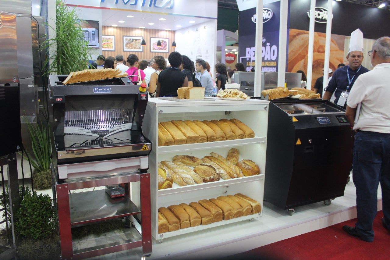 Um grupo de pessoas está em volta de uma vitrine de pães em uma padaria.