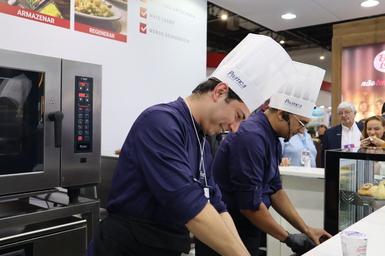 Dois homens usando chapéus de chef estão trabalhando em uma cozinha