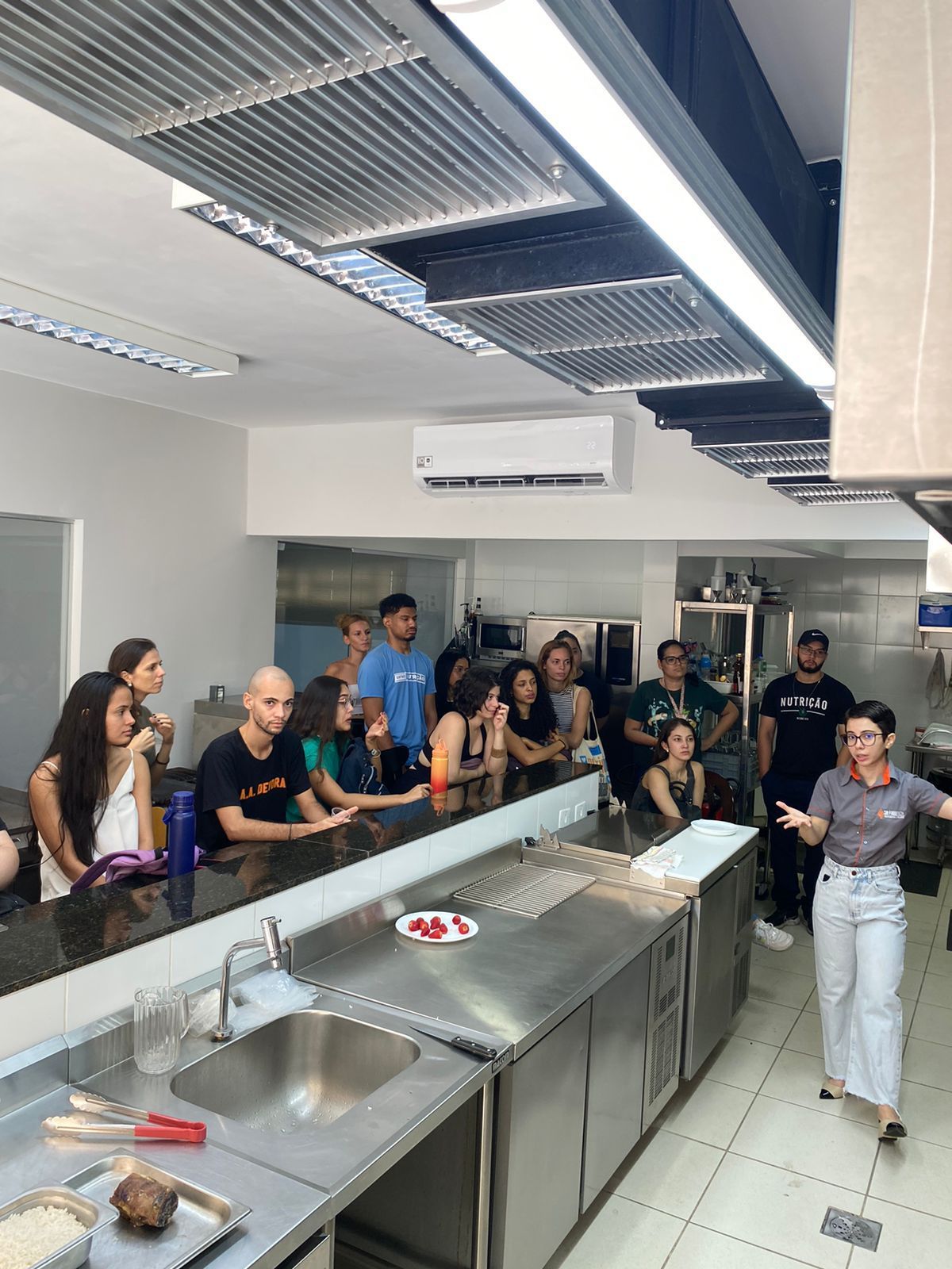 Um grupo de pessoas está de pé ao redor de um longo balcão em uma cozinha.