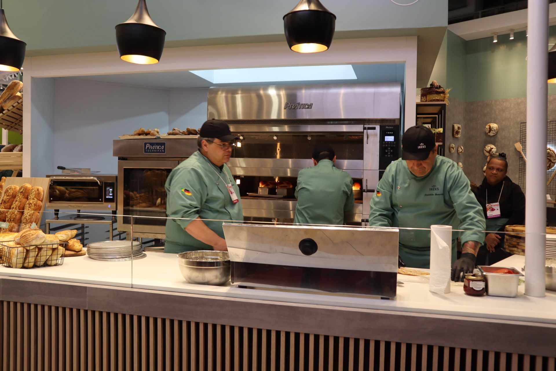 Dois homens de uniforme verde estão trabalhando em uma cozinha