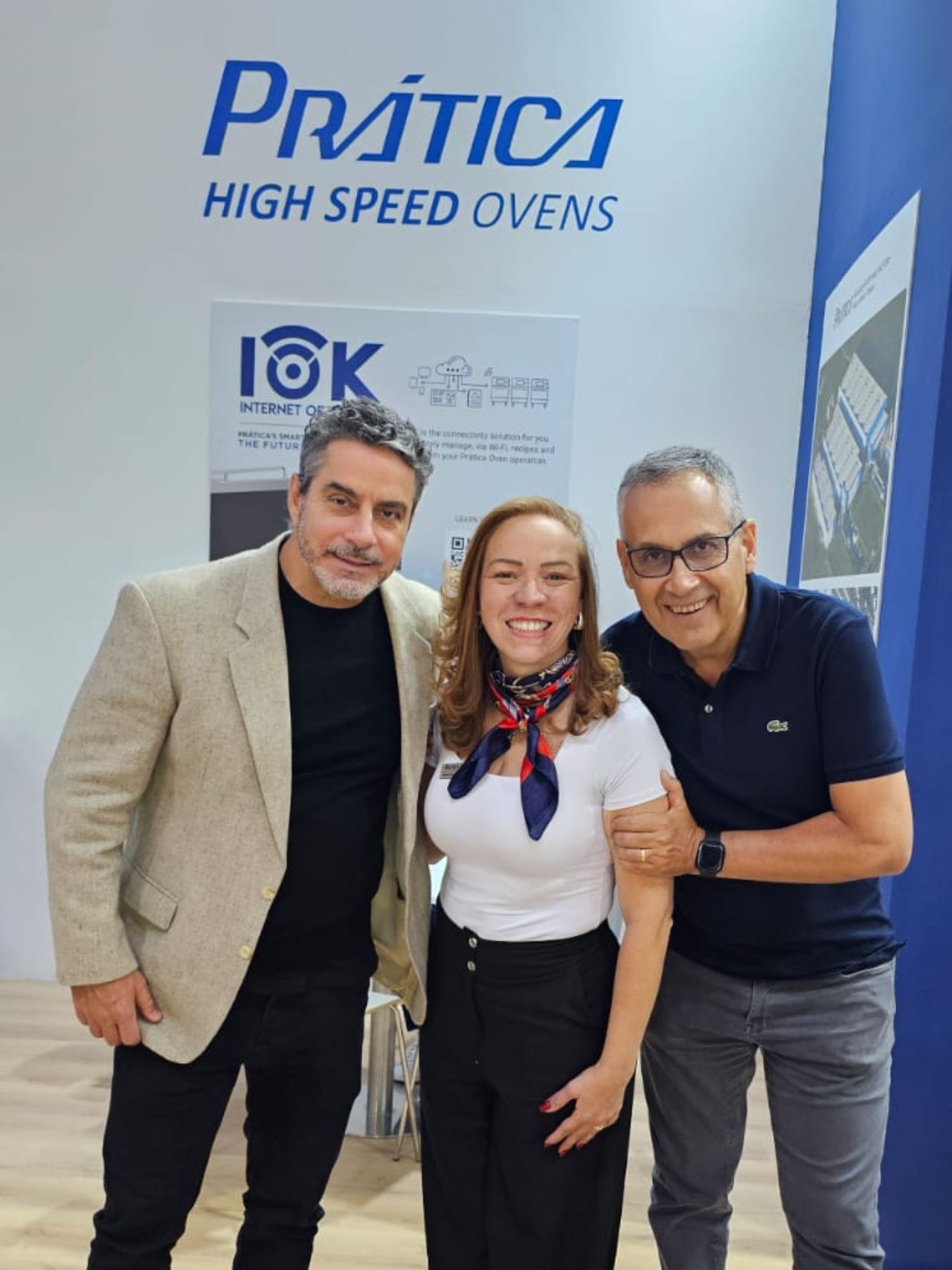 Três pessoas sorrindo em frente a uma placa “Fornos de Alta Velocidade Pratica”.