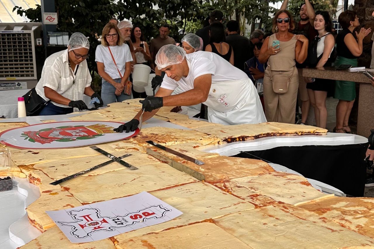 Chef cortando um pão sírio gigante enquanto a multidão assiste. Ambiente externo.