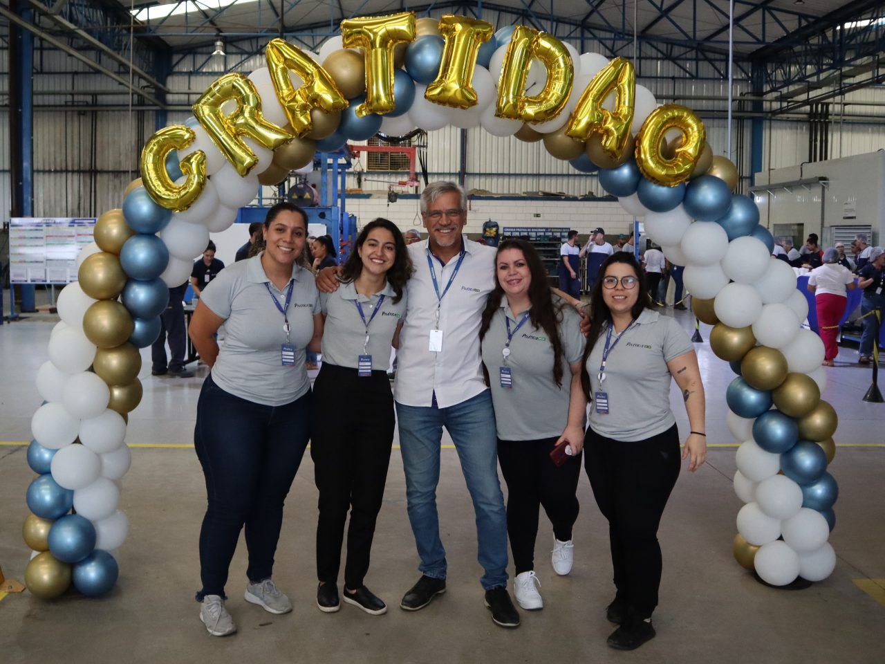 Um grupo de pessoas está posando para uma foto sob um arco de balões que diz gratidao.