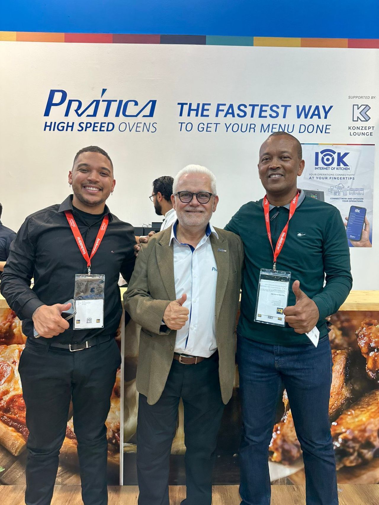 Três homens estão posando para uma foto em frente a uma placa que diz pratica a maneira mais rápida de fazer sua refeição.