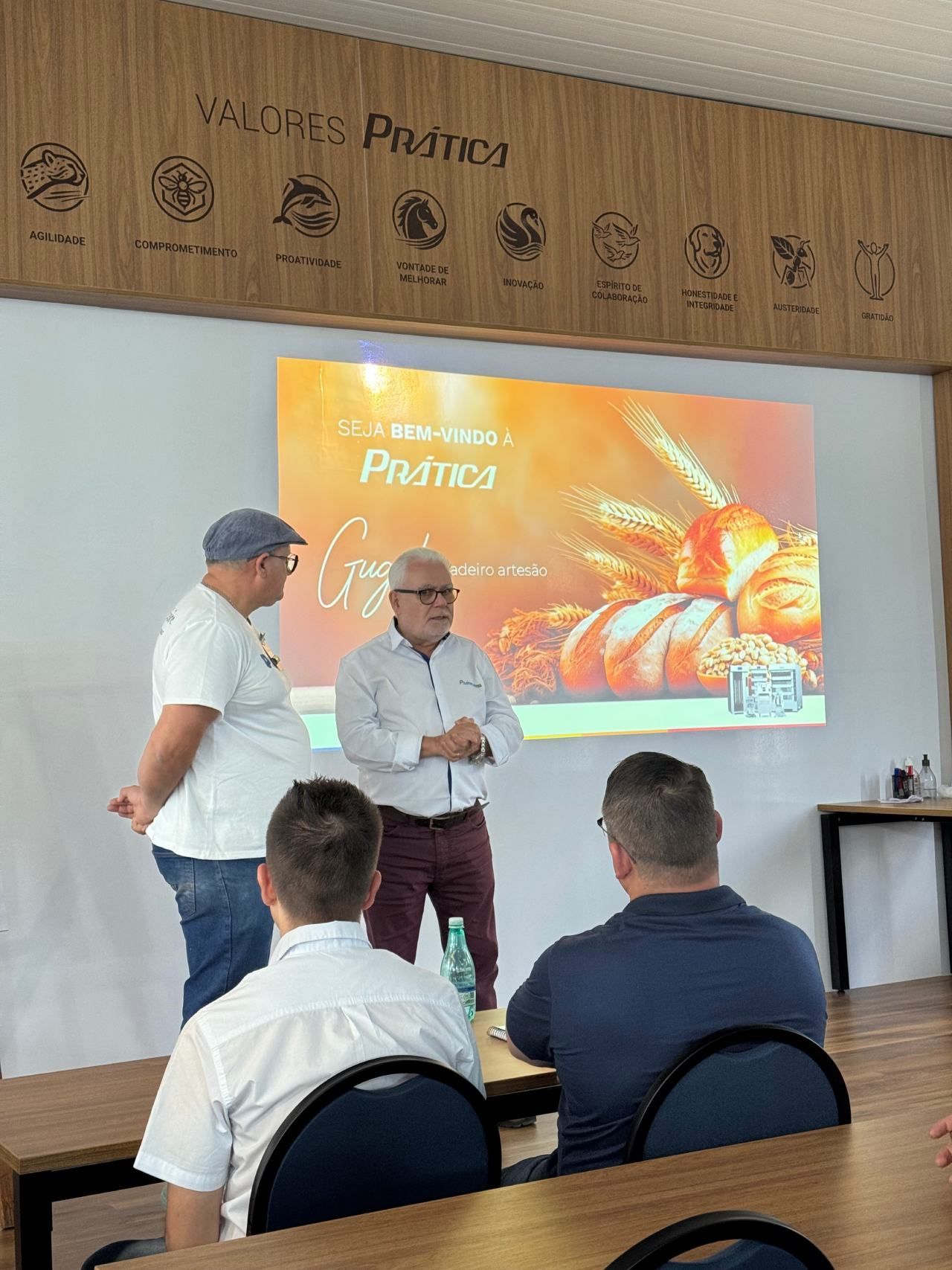 Um grupo de homens está sentado em mesas em frente a uma tela de projetor.