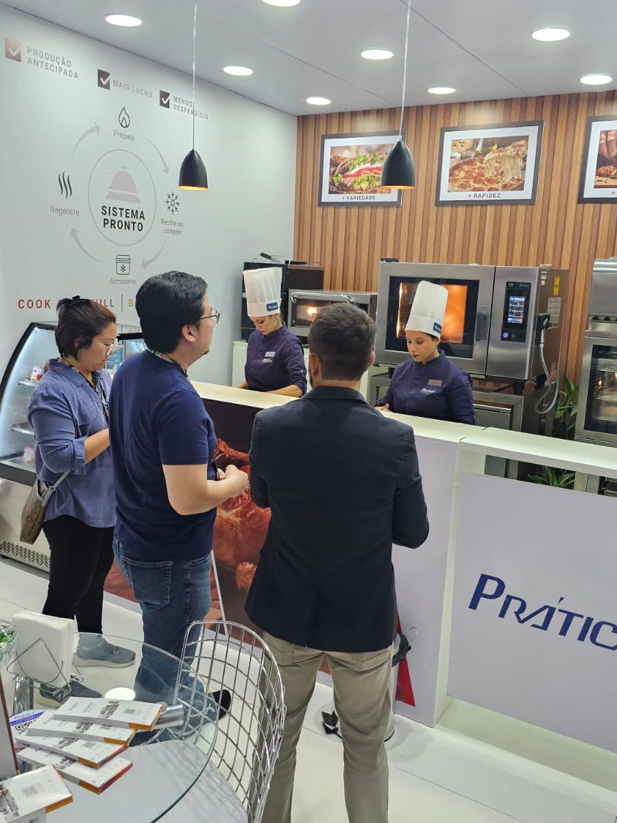 Um grupo de pessoas em pé ao redor de um balcão que diz pratika