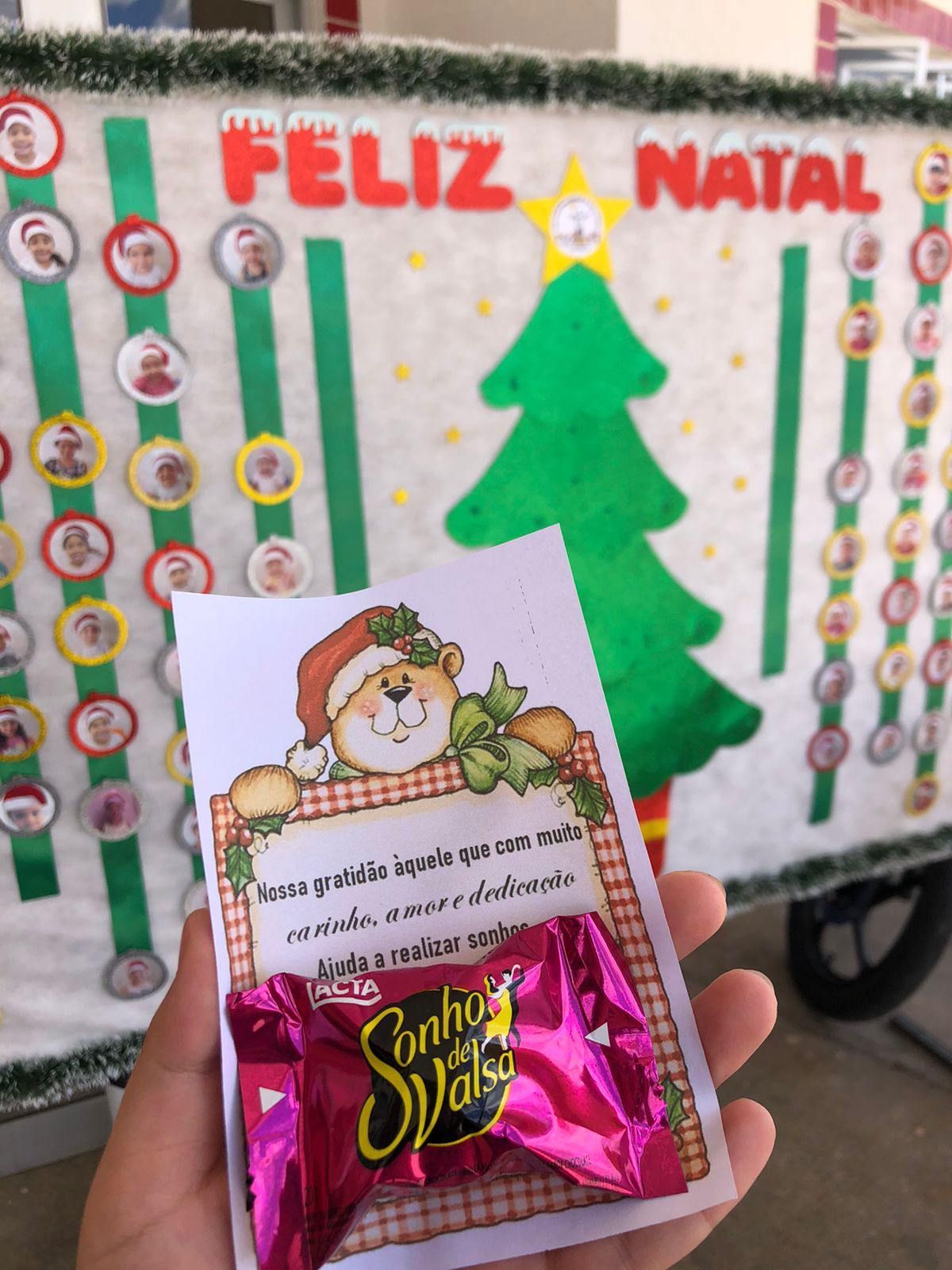 Uma pessoa segurando um doce em frente a uma placa que diz feliz natal