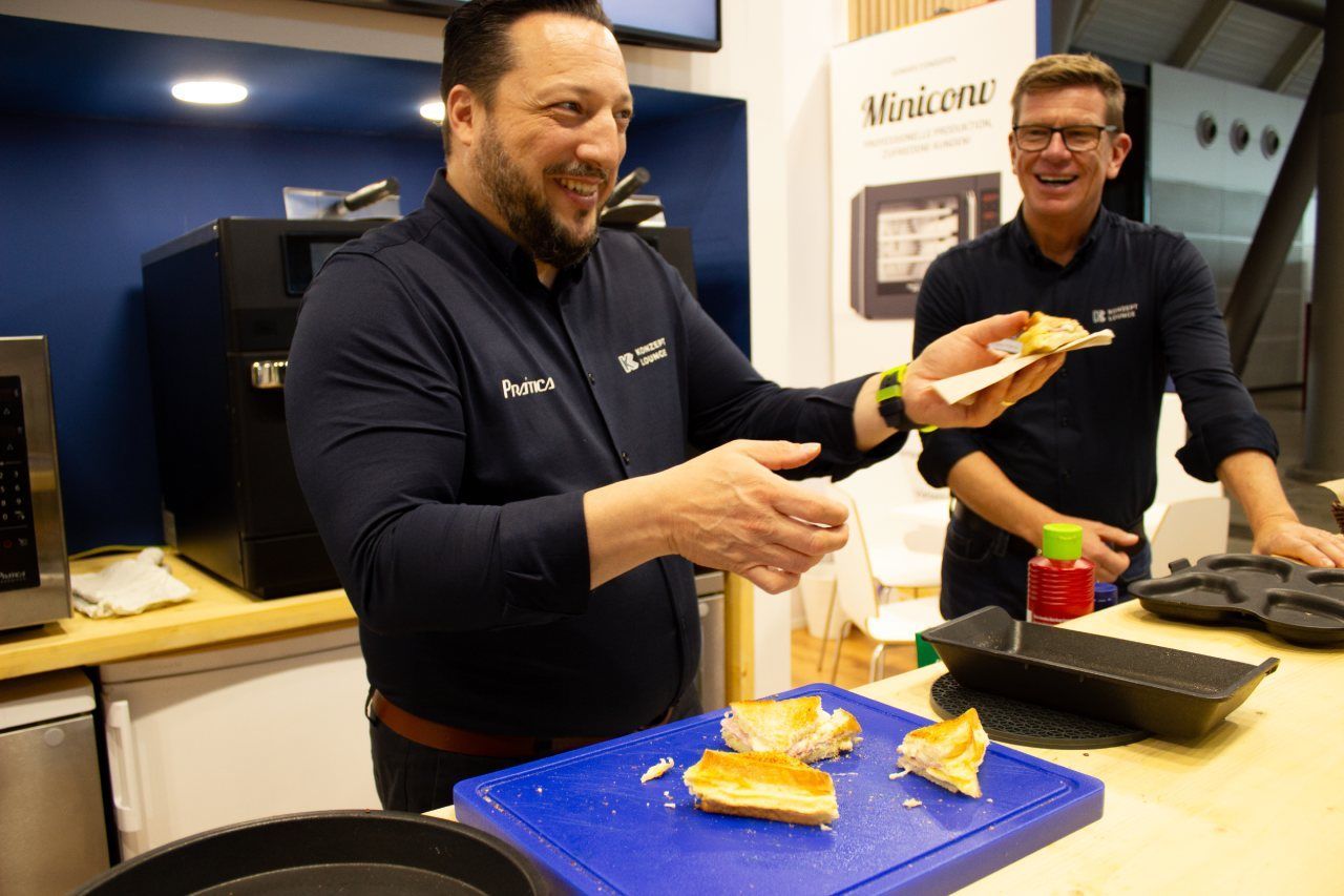 Dois homens estão em pé na cozinha comendo comida em uma tábua de corte.