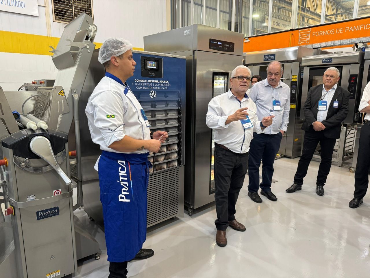 Chef demonstrando forno comercial para grupo em uma feira comercial, ambiente de padaria.