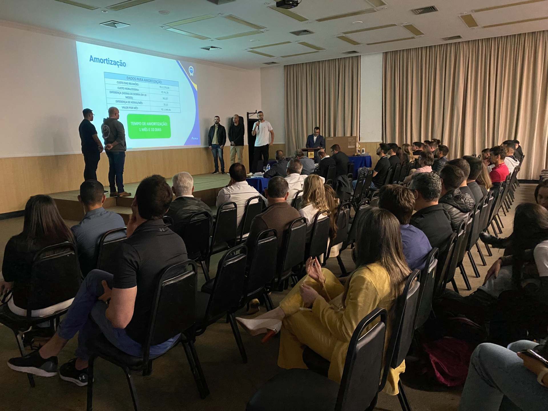Um grupo de pessoas está sentado em cadeiras em uma sala de conferências assistindo a uma apresentação.