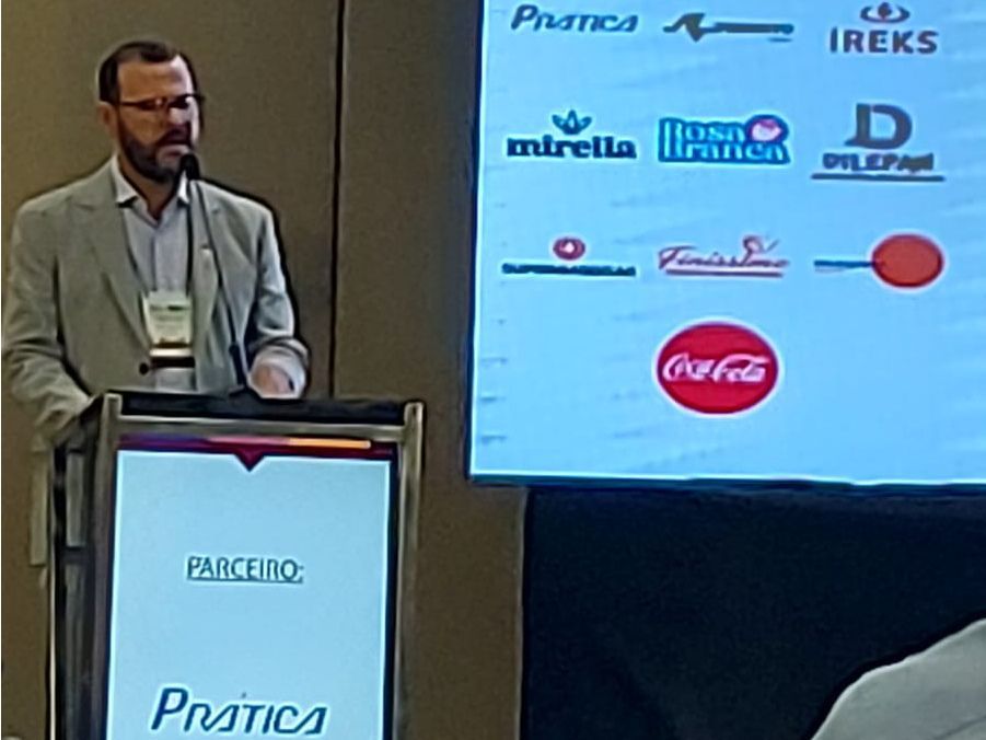 Um homem está em um pódio em frente a uma tela que diz prática