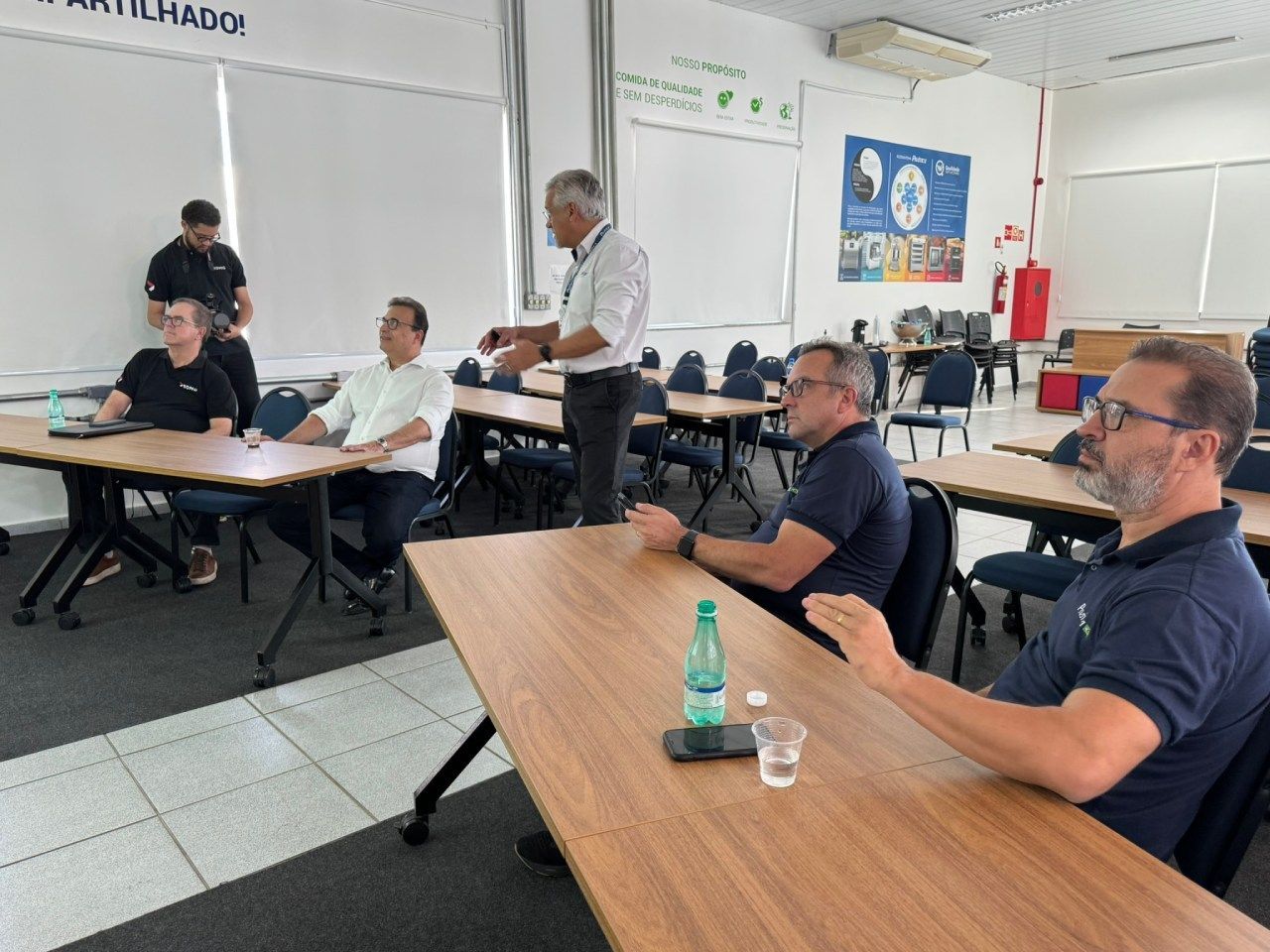 Um grupo de homens está sentado em mesas em uma sala.