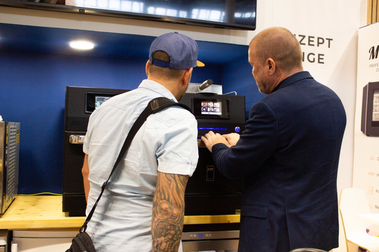 Dois homens estão olhando para uma máquina em uma cozinha.