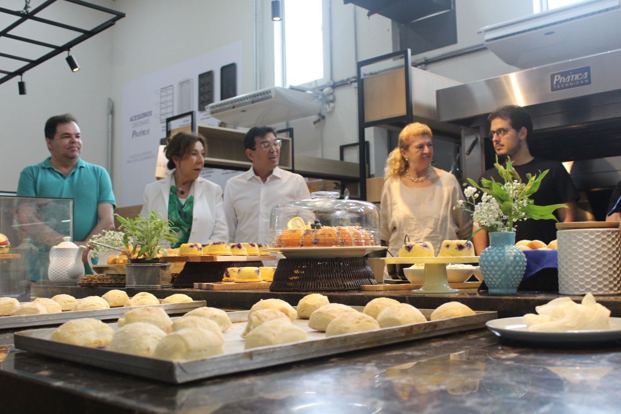Um grupo de pessoas está em pé ao redor de uma mesa com bandejas de comida sobre ela.