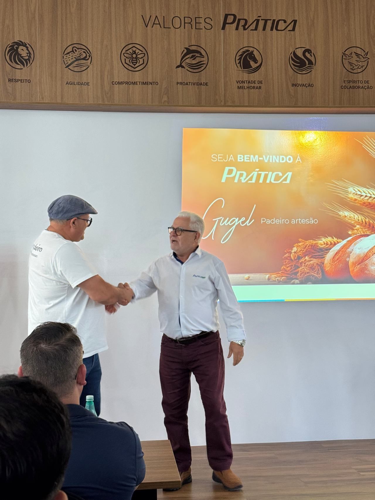 Dois homens apertam as mãos em frente a uma tela de projetor.