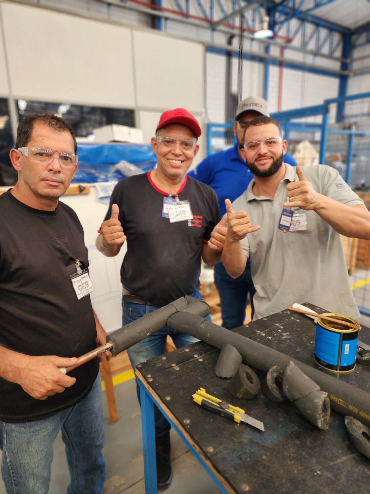 Três homens estão dando um sinal de positivo em uma fábrica