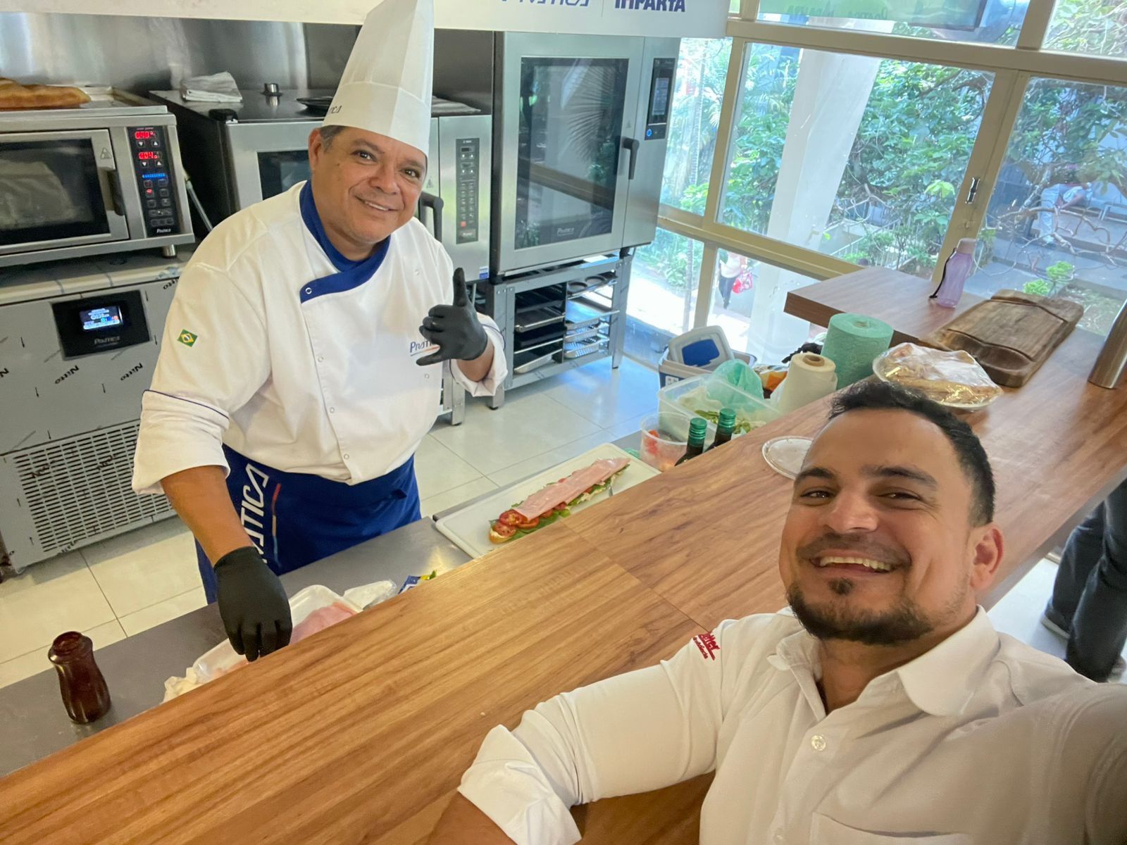 Um homem está sentado no balcão de uma cozinha ao lado de um chef.