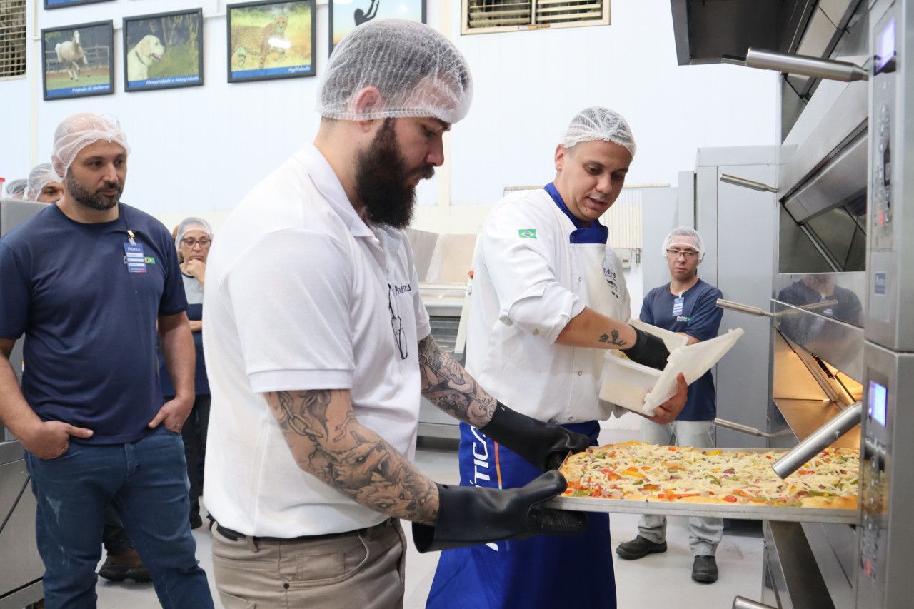 Um homem está segurando uma bandeja de pizza em frente a um forno.