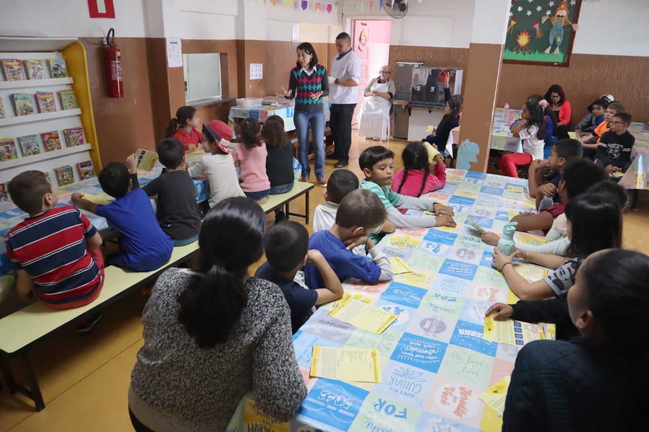 Um grupo de crianças está sentado em mesas em uma sala