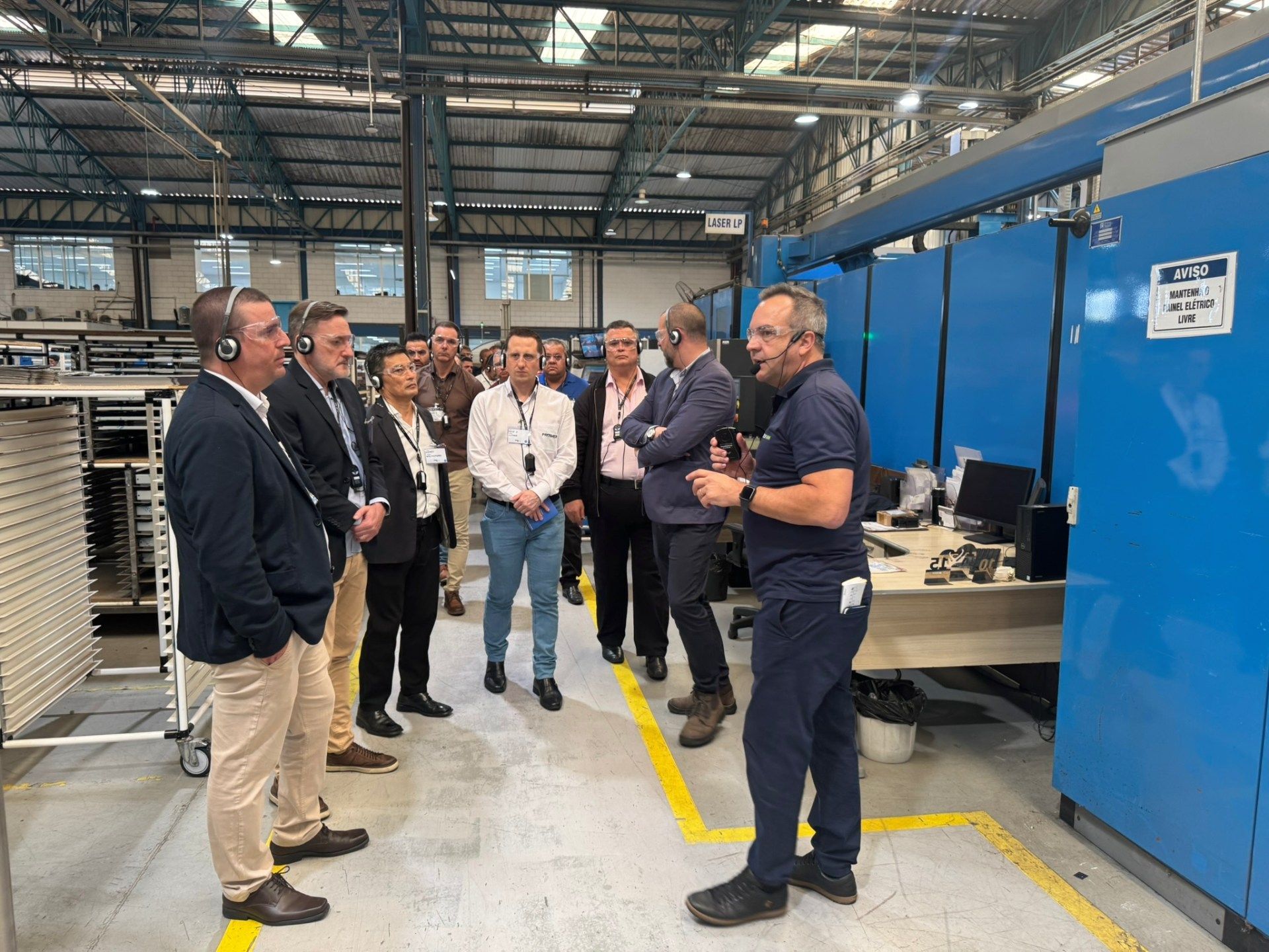 Um grupo de homens está em uma fábrica conversando entre si.