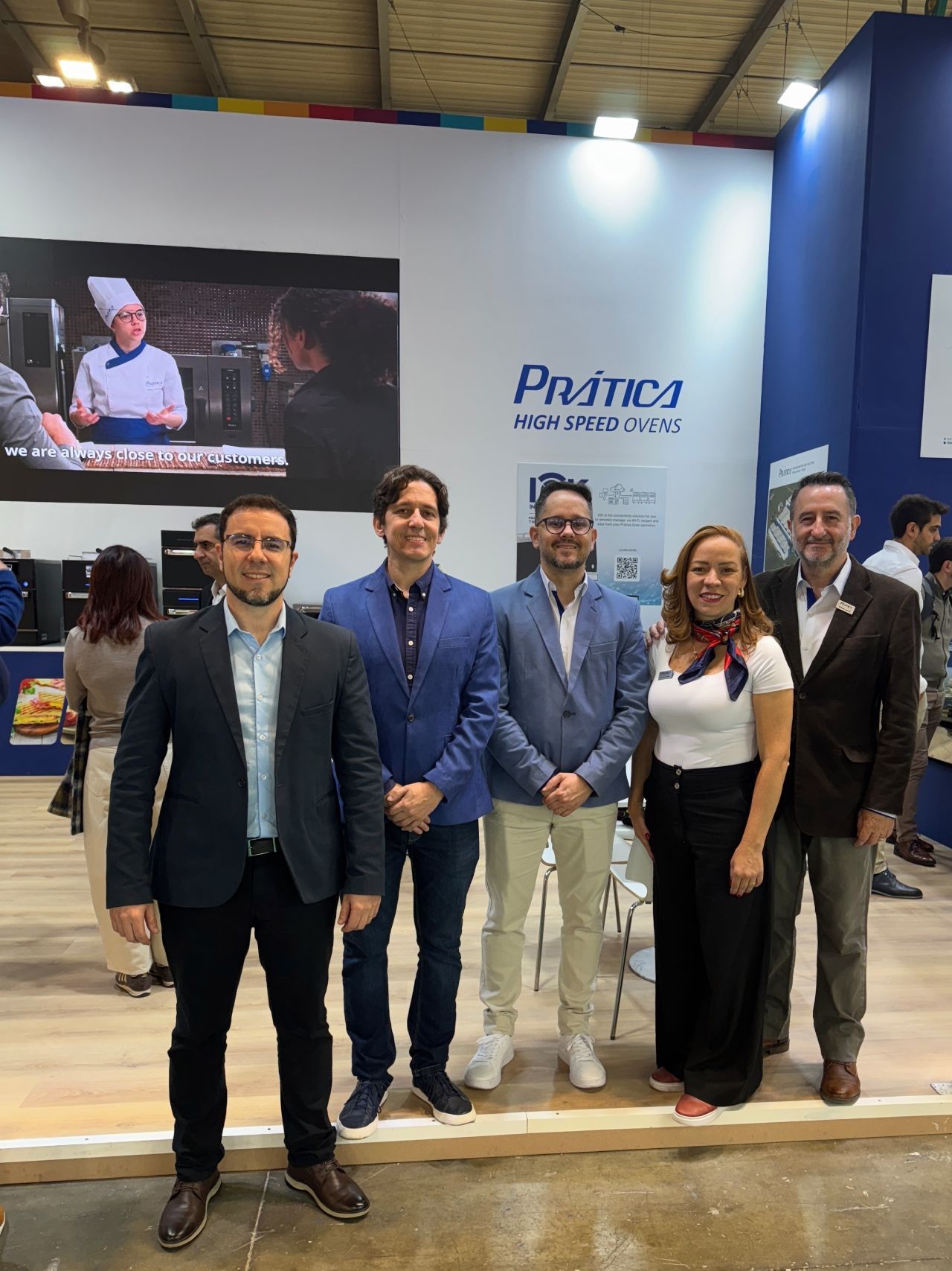 Grupo de pessoas em um estande de feira com o logotipo da Prática.