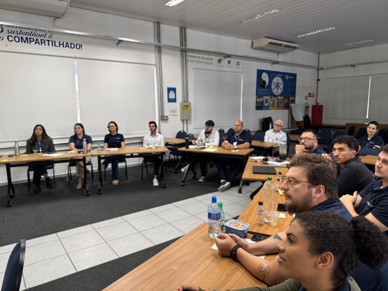 Um grupo de pessoas está sentado em mesas dispostas em fileiras