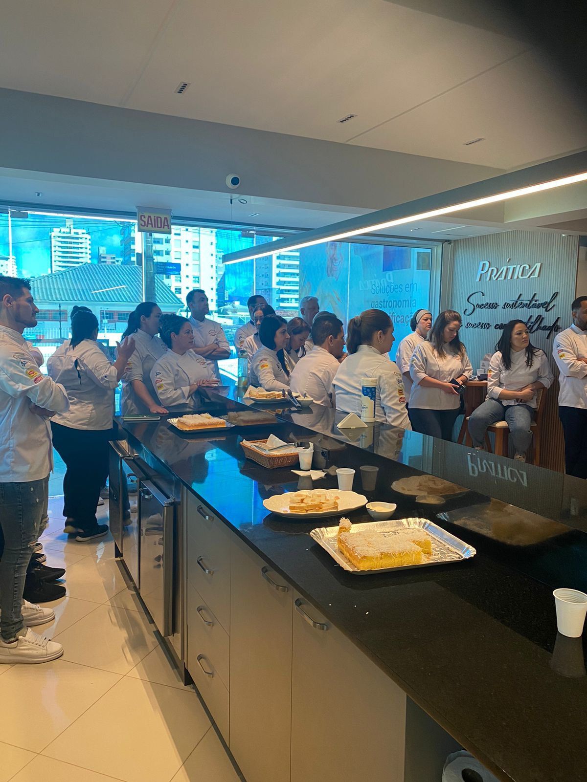 Um grupo de pessoas está em pé ao redor de um balcão na cozinha.