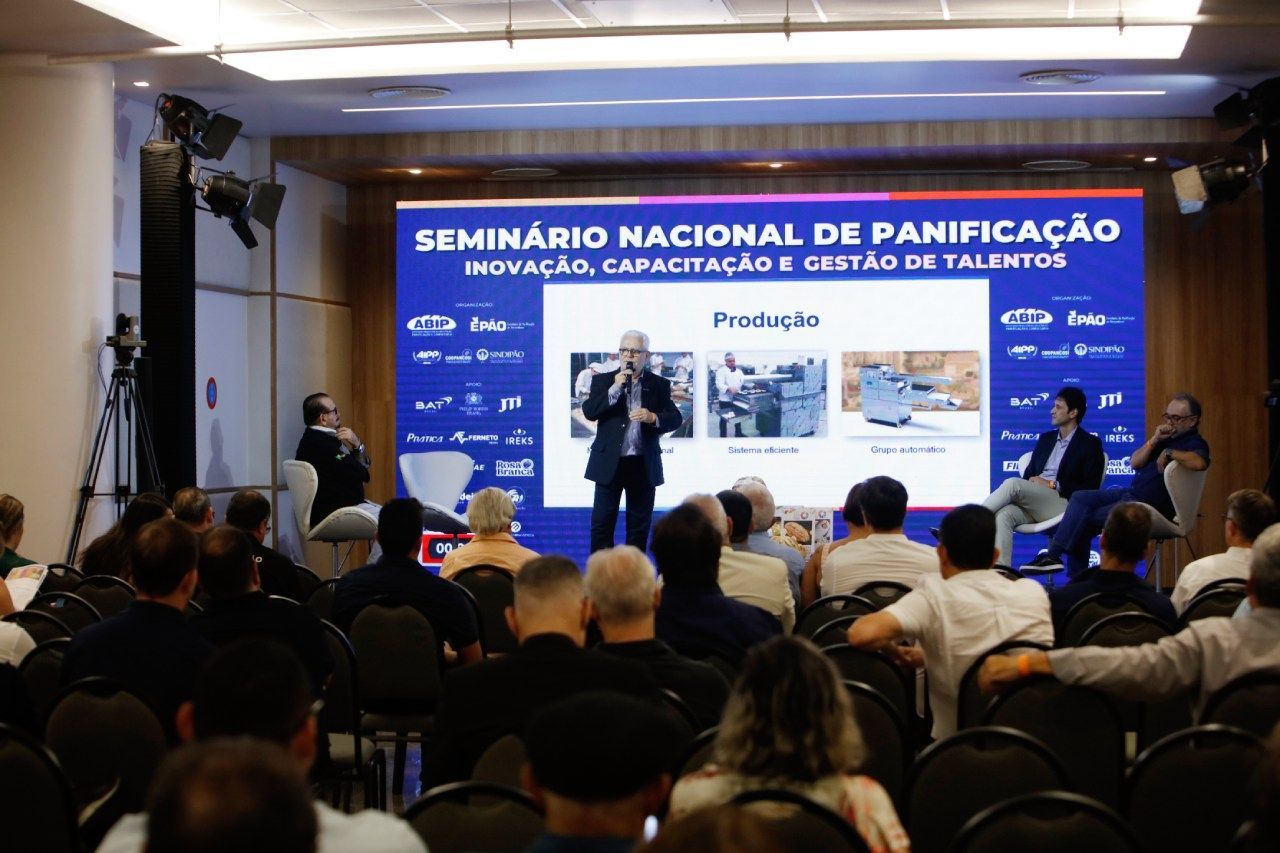 A group of people are sitting in front of a screen that says seminario nacional de panificação