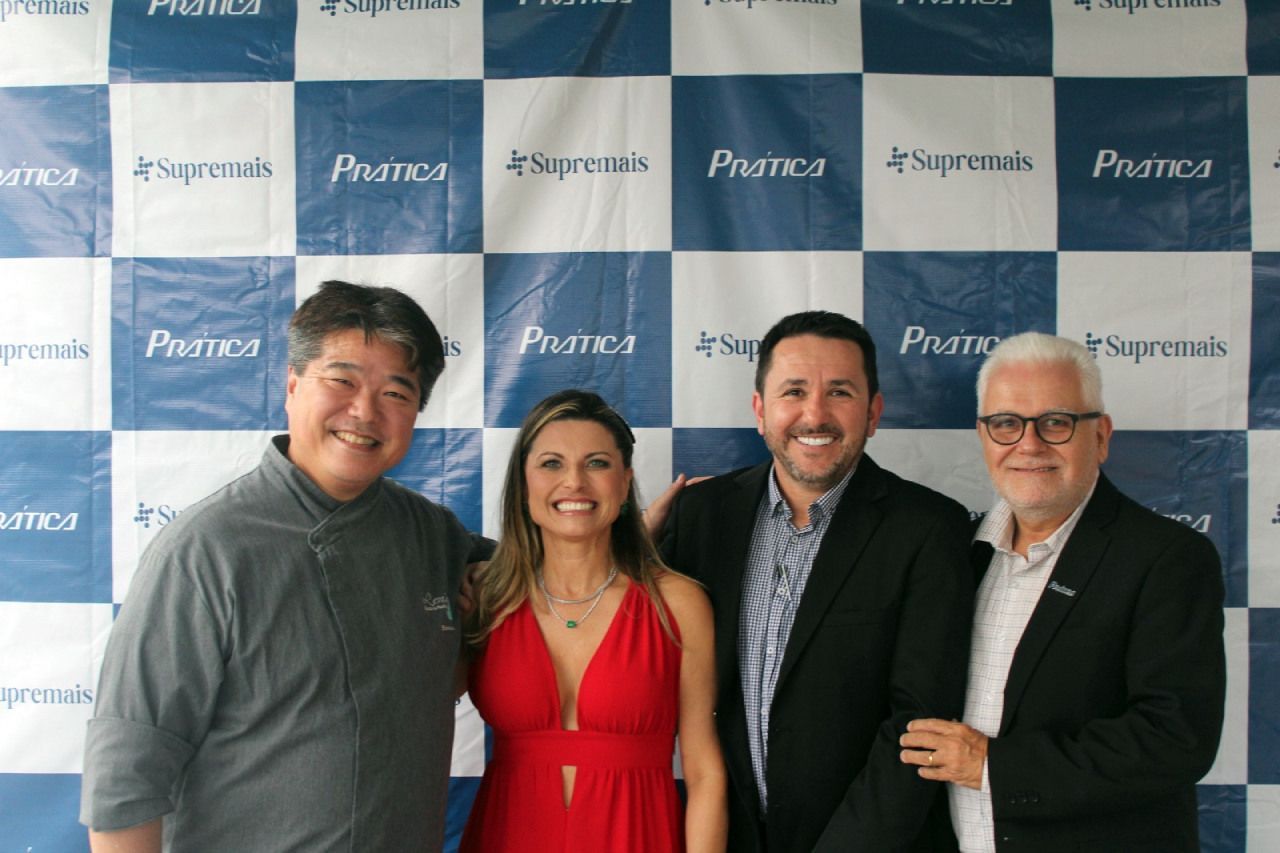 Um grupo de pessoas posando para uma foto diante de um cenário xadrez azul e branco.
