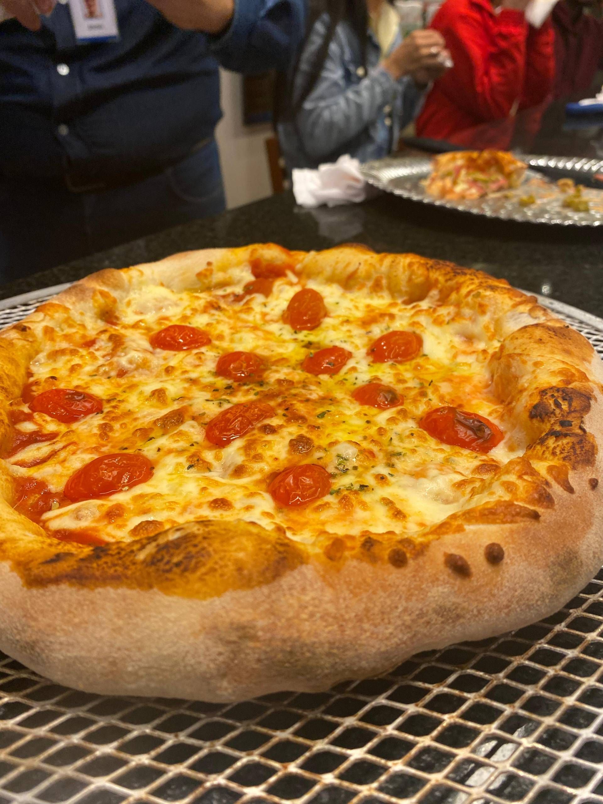 Uma pizza com queijo e tomate está sobre uma bandeja de metal sobre uma mesa.