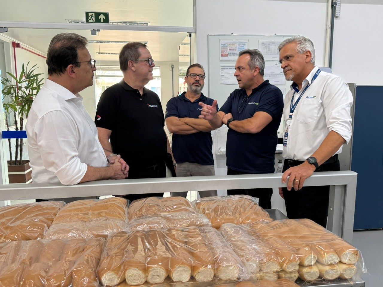Um grupo de homens está em pé ao redor de uma mesa com sacos de pão.