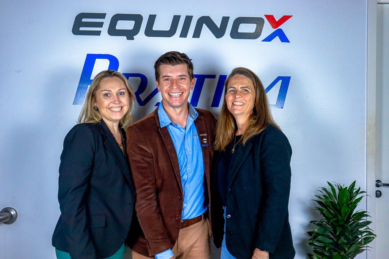 Um homem e duas mulheres estão posando para uma foto em frente a um signo de equinócio.