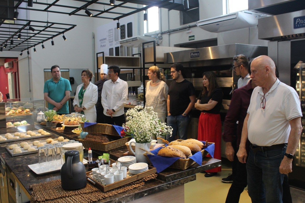 Um grupo de pessoas está em pé ao redor de uma mesa em uma padaria.