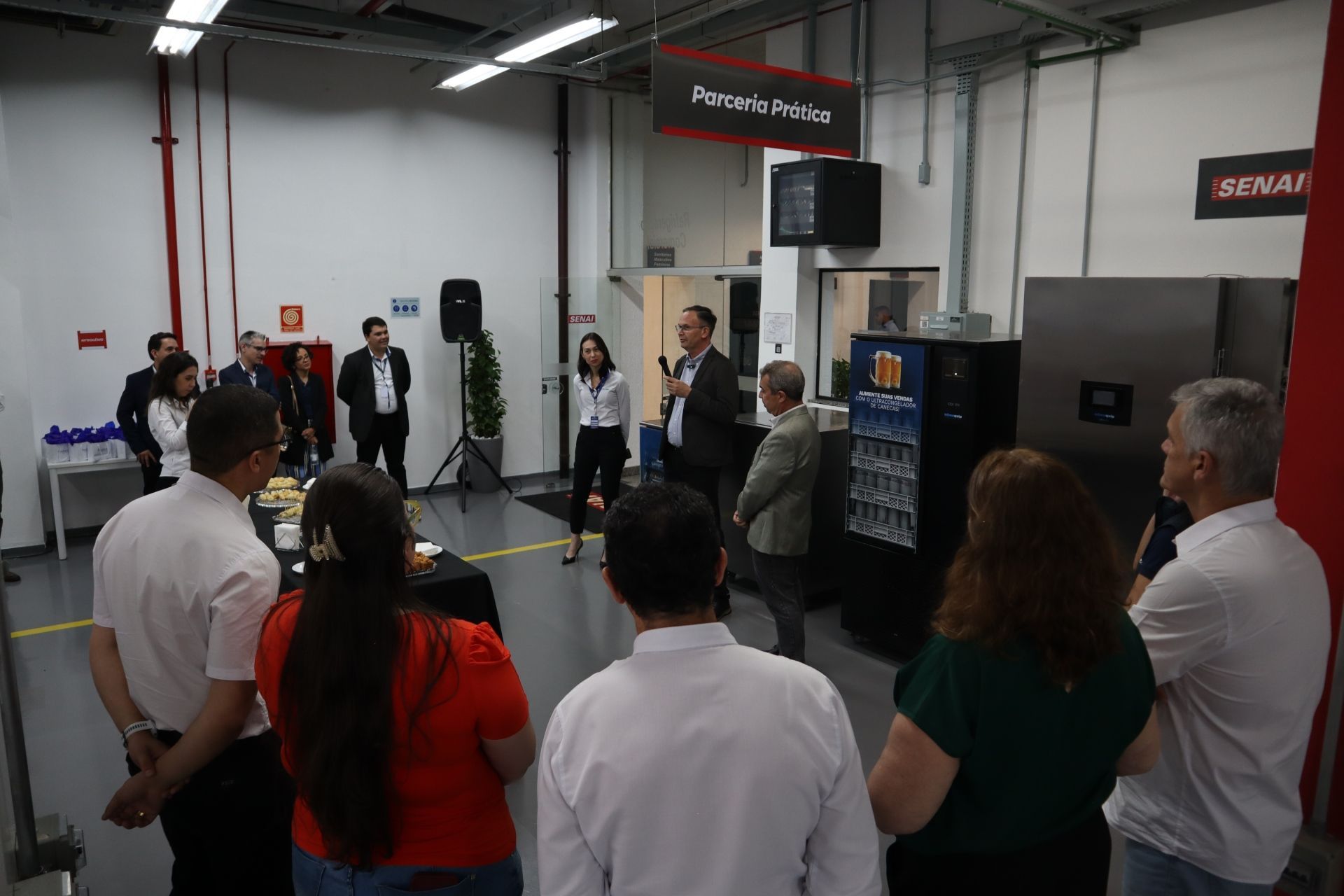 Um grupo de pessoas ouve um palestrante em um workshop com comes e bebes.