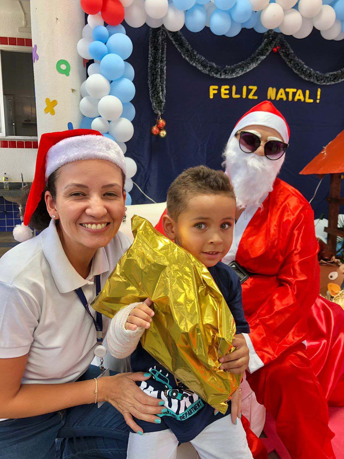 Uma mulher com um chapéu de Papai Noel está posando para uma foto com um garotinho fantasiado de Papai Noel.